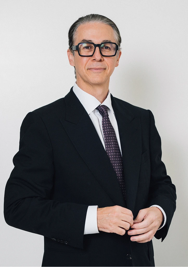 Professional portrait of Dr. Martin Jugenburg wearing a dark suit, white shirt, and patterned purple tie against a clean white background.