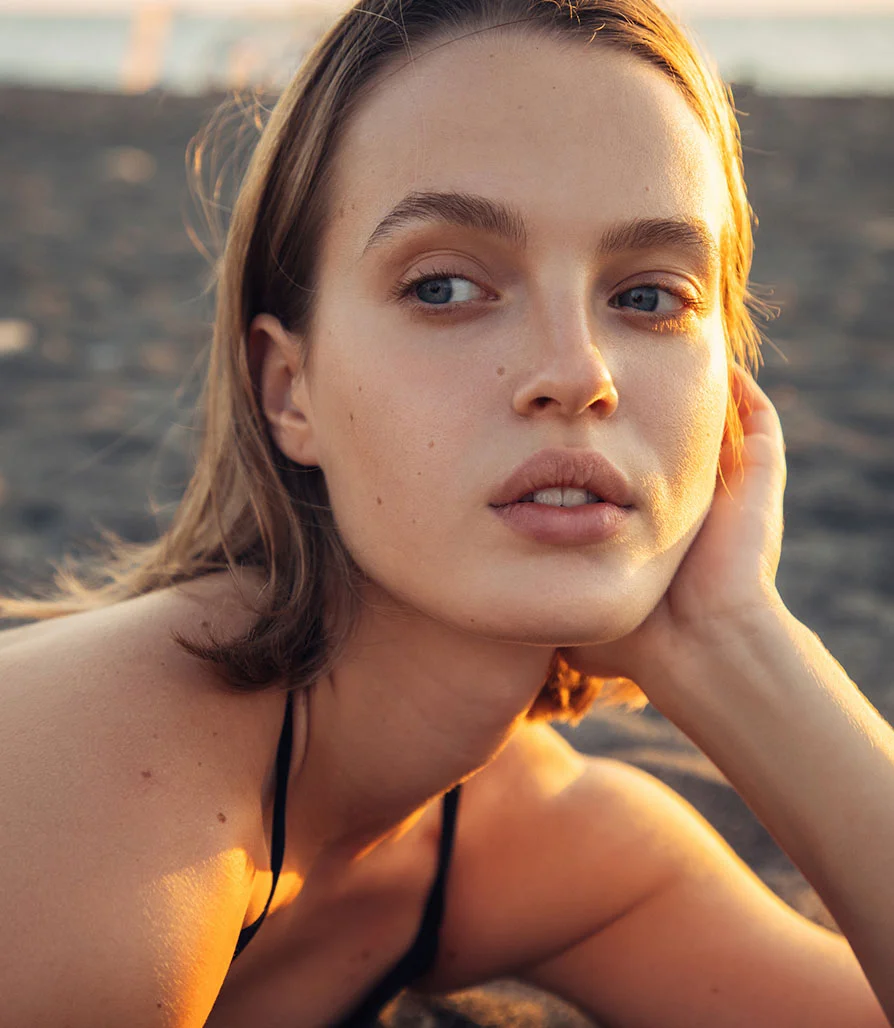 A natural, soft-lit portrait of a woman on a beach at sunset, emphasizing the shortened philtrum and enhanced upper lip visibility following a surgical lip lift.