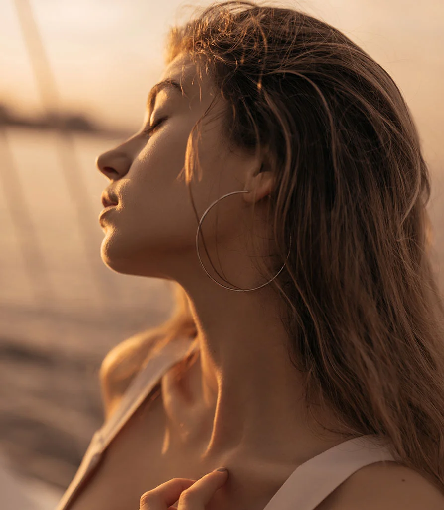 Profile view of a woman at sunset, highlighting a sharp, defined jawline and slender neck achieved through submental (chin) liposuction.